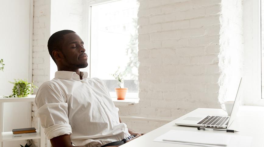 A black male meditating at his desk with his eyes closed.