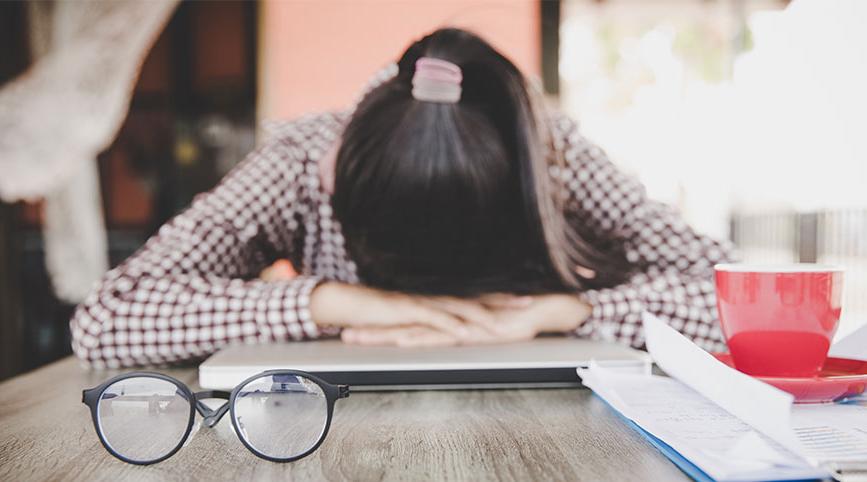 A female person has her head on her desk in frustration