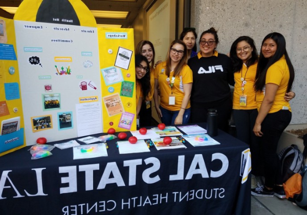 Six student interns in yellow shirts behind outreach table.